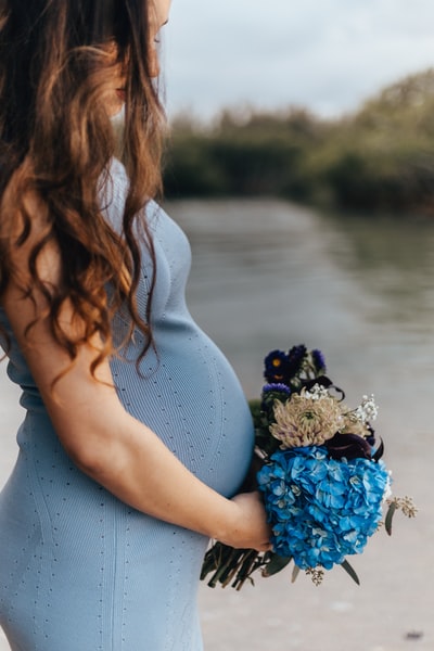 身着蓝色无袖连衣裙的孕妇手持一束鲜花